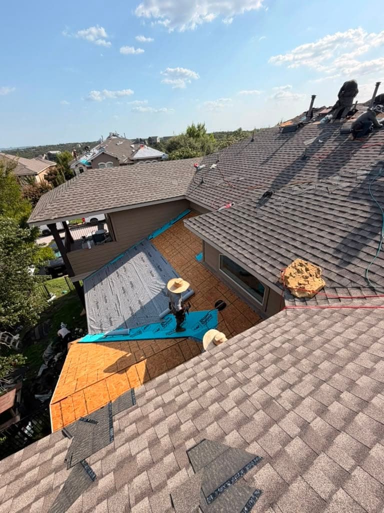 Elevated view across a multi-plane roof mid-build, crew working new decking and dry-in