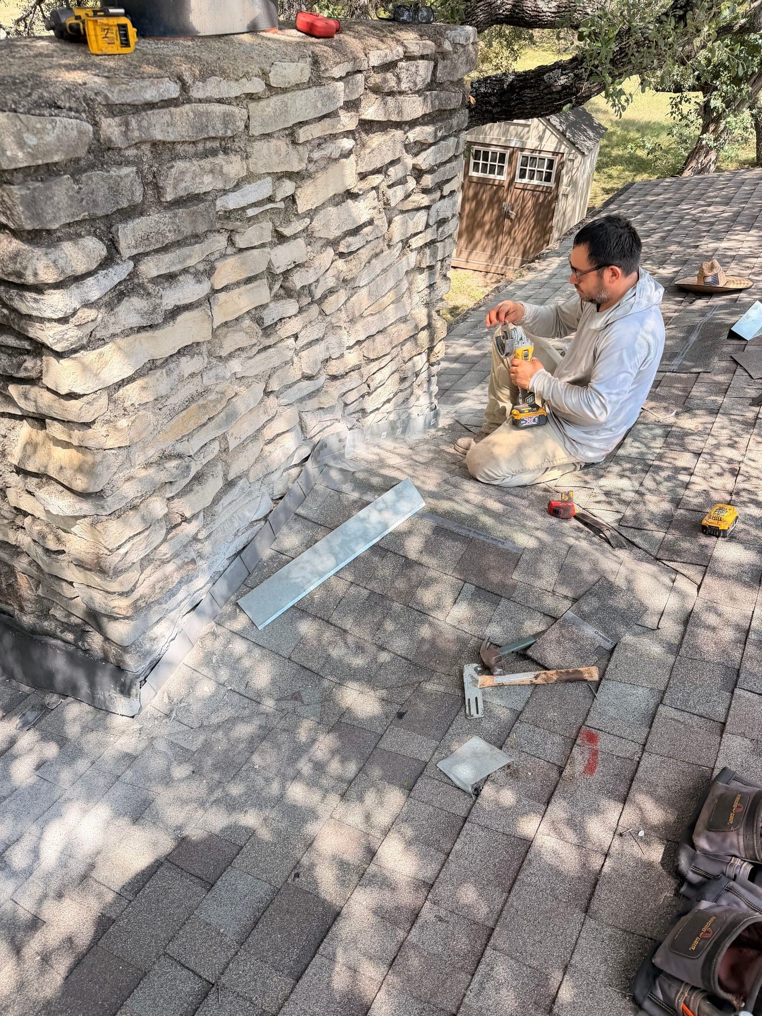 Crew member cutting chimney flashing on the roof, a new flashing pan already set tight against the stone