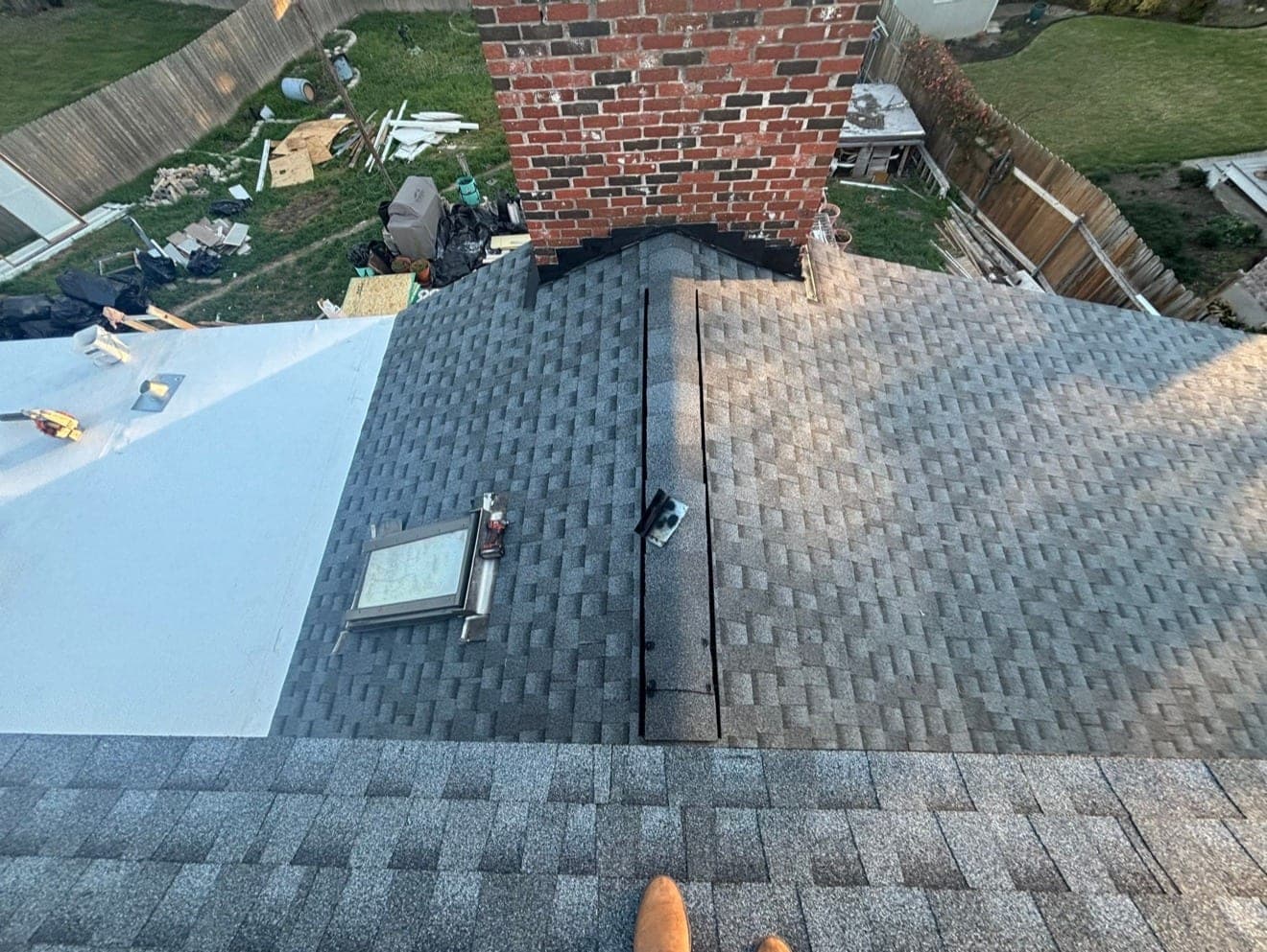 Low-slope white membrane meeting a new architectural shingle field at a brick chimney, skylight and ridge visible