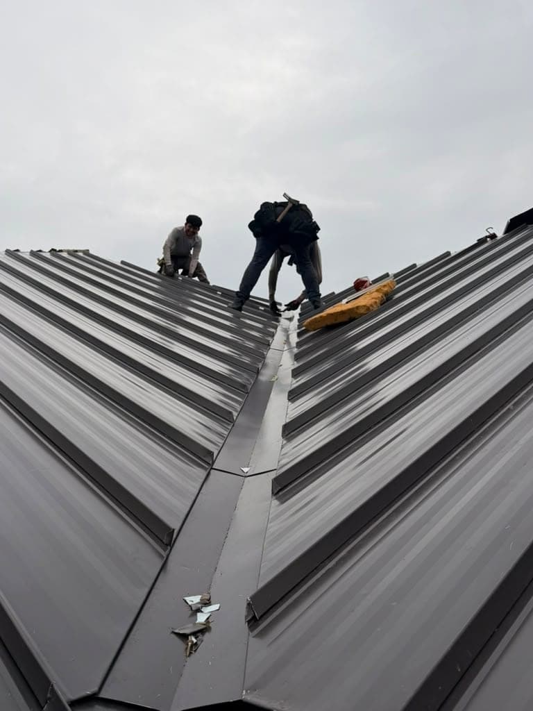 Two crew members working the ridge of a standing seam metal roof